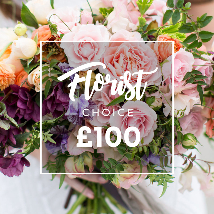 This image reads like a quiet love note from the garden: a hand-tied Florist Choice bouquet fills the frame, topped by a white rectangular overlay that states Florist Choice in elegant script, with CHOICE in smaller block letters beneath and ?100 displayed boldly at the bottom. Visually the bouquet is opulent yet unstudied - large, soft pink garden roses provide a plush core, their ruffled layers like well-made fabric. Deep plum, almost wine-coloured hellebore-like blooms collect toward the lower left, balancing the palette with dramatic tones, while pale purple-and-white striped sweet peas thread delicate highlights through the arrangement. Peach and coral ranunculus add sunlit, layered warmth, and creamy white accent blooms lift the composition with subtle brightness. Fresh, varied greenery - slender, trailing vines and broader textured leaves - is woven throughout, giving a natural, garden-style fullness and a sense of movement. A pair of hands supports the trimmed stems at the base; the faint white sleeve and blurred, light-coloured background keep attention on the flowers themselves. The lighting is soft and directional, catching sheen on petals and revealing tactile details that invite touch. This bouquet feels right for an intimate wedding, a meaningful anniversary or a thoughtful luxury gift delivered within local streets like Fortess Road or along the Tufnell Park high street - a florist-selected composition that promises seasonal variety and careful handling.