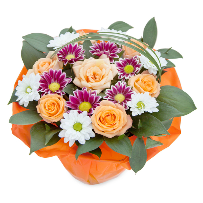 Overflowing with cheerful flora and artistic flair, this bouquet is elegantly captured from above, illuminated in clear, natural light-much like a market display near Tufnell Park Station. Dominated by open peach and tangerine-hued roses, their petals unfurl with classic sophistication, embracing the soft romance found in local garden squares. Nestled among them are round, daisy-like chrysanthemums: striking in their crisp white with vivid green centers, and mesmerizing in their rich magenta and purple shades, each with a yellow or lime-green eye. The overall composition is made lush with an abundance of dark, glossy ruscus foliage, which weaves through the arrangement, echoing the hidden greenery of Lady Somerset Road's gardens. Adding finesse, a slender loop of vibrant green decorative grass sweeps gracefully above, giving a final touch of contemporary design. The bouquet's base is wrapped snugly in translucent orange cellophane, gently crinkled to accentuate the structure and bring cohesion to the warm rose tones. Every element of this hand-crafted floral display, available for same-day delivery across Tufnell Park and neighbouring Holloway, is chosen to conjure feelings of happiness, appreciation, and celebration-a true testament to the floristry expertise and thoughtful service at Flowers Tufnell Park.