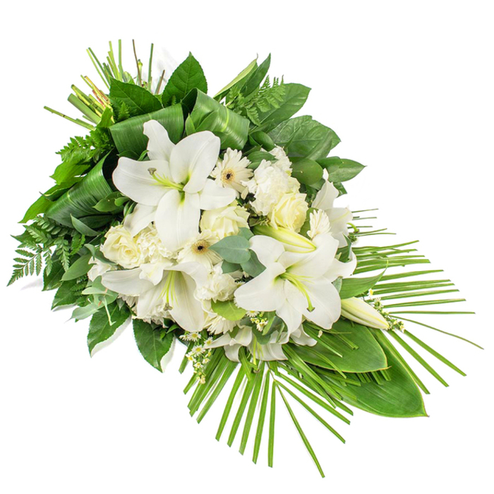 An elegant, elongated funeral arrangement in pristine white and layered green is photographed against a pure white background, designed as a one-sided display that appears to cascade gently from left to right. At its focal point, several large white lilies command attention, their generous, trumpet-shaped blooms fully open, with smooth petals that curl slightly at the tips and enclose pale green and yellow stamens. Some lily buds remain closed, tapered and upright, promising beauty that will unfold in the coming days. Surrounding the lilies is a thoughtful mix of classic white flowers: soft roses in varying stages of bloom, ruffled carnations with their intricate petal edges, and neat white Gerbera-style daisies with dark or soft yellow centres, each adding its own character and depth. Fine stems of tiny white filler blossoms are threaded between the larger blooms like stars scattered across a calm sky, adding a light, airy texture that never overwhelms. The lush foliage beneath is built from several greens: broad, glossy leaves give a solid foundation; light, feathery fern fronds contribute a gentle frill; and rounded eucalyptus leaves introduce a cool, silvery-green shade. At the upper portion of the design, long narrow leaves are carefully folded and tied into sleek vertical shapes, giving a tailored, modern edge. From the lower right, numerous slender palm fronds fan outward in a graceful arc, extending the form into a teardrop-like spray that feels both modern and dignified. The whole arrangement suggests peace, reverence, and quiet remembrance, the sort of thoughtful tribute that might rest beside a coffin in a Tufnell Park chapel or accompany a final goodbye at a local cemetery, thoughtfully prepared by experienced hands who understand the comfort flowers can bring.