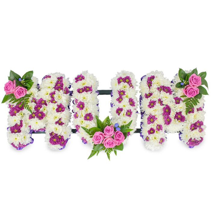 This heartfelt floral tribute spells out MUM in three large, sculpted capital letters set against a simple white background so the textures and colours read clearly. Each letter is lovingly formed from a voluminous bed of pristine white chrysanthemums whose clustered petals create a plush, cushiony surface that invites touch and conveys serenity. Threaded through that white field are accents of deep magenta and purple pom-like chrysanthemums, forming soft patches that add dimension and a gentle visual rhythm across each letter. The tribute is punctuated by three discreet rose groupings: a small, elegant cluster of two to three bright pink spray roses and accompanying fern leaves sits at the top left corner of the first M; the central U cradles a larger bouquet of roughly four to five pink spray roses with abundant greenery in its lower curve; the right-hand M mirrors the left with a matching rose and foliage cluster. Deep green ferns and other leafy stems frame these focal points, and tiny blue filler flowers peek through to add a cool highlight. A subtle, narrow dark bar runs horizontally behind the letters, providing implied support and a composed silhouette. The arrangement reads as both an intimate farewell and a celebration of memory - refined, traditional, and quietly expressive. In the context of a Tufnell Park memorial service, perhaps near the tube or a local chapel on Junction Road, this piece would bring a calming scent of chrysanthemum and rose and a steady, comforting presence for family and friends during moments of remembrance.