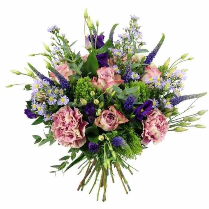 A luxurious, dome-shaped bouquet filled with shades of pink, mauve, purple, and vivid green is displayed against a crisp white backdrop, the kind of arrangement you might see resting on a polished table in a Tufnell Park townhouse. At its centre, soft pink roses unfold gracefully, some with petals still wrapped tightly around the bud, others opening wide so that each layered petal can be seen, the colour subtly deepening toward the heart of the bloom. Interspersed are large, frilled carnations in dusty rose and purple-mauve, their ruffled petals adding a sense of volume and plush texture that contrasts beautifully with the smoother rose petals. Vertical accents come from elegant spikes of deep lavender-blue Veronica, their slim, tapering forms drawing the eye upward and adding a refined, architectural structure to the bouquet. Between these taller stems, clusters of rich purple lisianthus and small, daisy-like lavender asters with soft yellow centres scatter delicately throughout, creating a soft, clouded fill that keeps the design feeling light rather than heavy. The greens are just as carefully chosen: silvery-green eucalyptus leaves arc gently around the blooms, while bright lime-green filler such as green trick dianthus or sedum punctuates the arrangement with lively, almost glowing touches of colour. Together they frame the flowers and enhance the sense of freshness, as if the bouquet has just been gathered from a garden near Tufnell Park or the paths leading toward Hampstead Heath. The stems are clearly visible beneath the flowers, neatly trimmed and hand-tied into a tight, rounded bundle, ready for a vase on a dining table or bedside. The overall impression is one of thoughtful elegance and heartfelt sentiment, making it fitting for luxury flower delivery, anniversaries, birthdays, or simply a beautiful surprise for someone living in or around Tufnell Park.