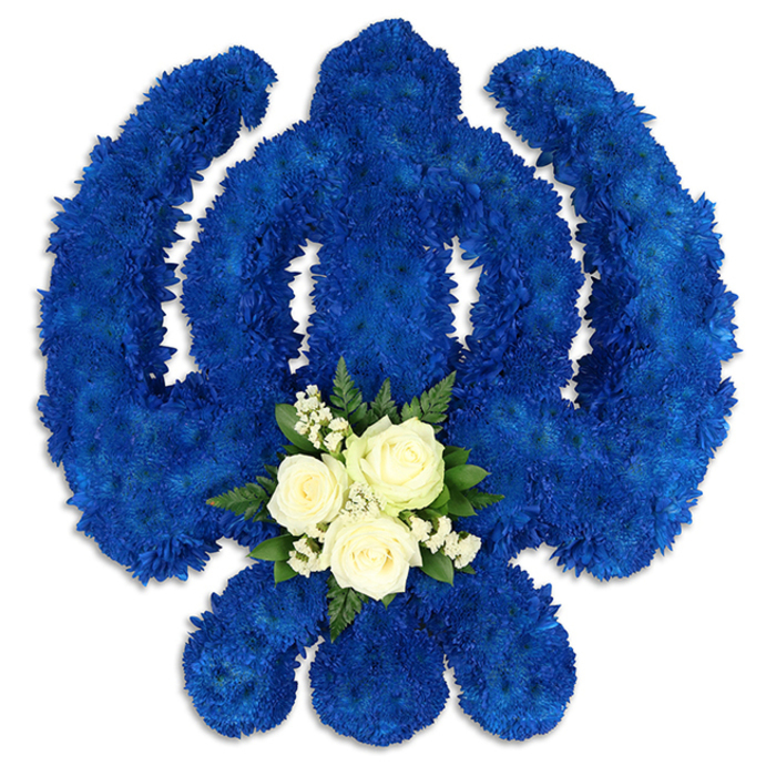 An elaborate floral representation of the Sikh Khanda symbol is displayed against a spotless white background, its strong lines and curves brought to life entirely in flowers. The complete emblem-the central double-edged sword, the surrounding chakkar, and the two outward-sweeping kirpans-is meticulously outlined in deep royal blue chrysanthemums or similarly clustered blooms. Each tiny floret is positioned closely to the next, creating an unbroken field of blue that feels rich and velvety to the eye, like a ceremonial cloth laid out with care. Light glides over the rounded tops of the flowers, catching subtle highlights along the outer arcs and leaving gentle, shaded contours in the recesses, which gives the tribute a sculpted, three-dimensional quality. At the base of the central sword, a contrasting cluster of fresh white and green blooms forms a poignant heart to the design. Three white roses sit at the centre, their petals firm but softly layered, edged by fine sprigs of white filler flowers-similar to baby's breath-that add a lace-like delicacy. Around them, small sprays of dark emerald foliage frame the cluster, infusing the design with a hint of garden freshness, like greenery seen along the paths of Tufnell Park Fields on a quiet morning. The deep blue of the Khanda evokes strength, justice, and devotion, while the white accent speaks of peace, purity, and a gentle farewell. This thoughtful floral tribute would feel at home at a Sikh funeral or remembrance service for a Tufnell Park family, a carefully crafted expression of respect for both the departed and their living faith, prepared by local florists who understand the significance of every petal and line.