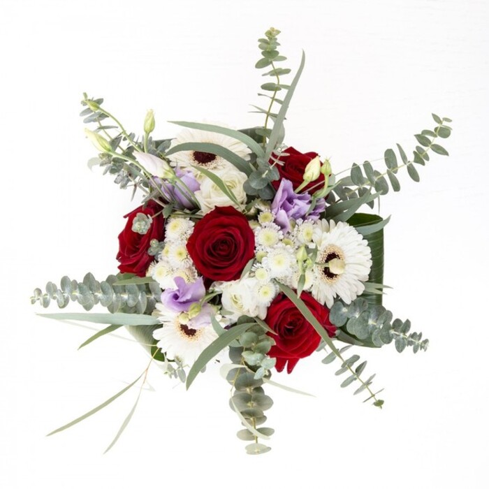 Viewed from above on a pristine white backdrop, this bouquet from a skilled Tufnell Park florist unfolds as a visual sonnet-each flower an essential note in its harmonious composition. The deep, plush red roses anchor the piece, their velvet petals curled protectively, exuding passion and an air of timeless romance. Interspersed, three bold white gerbera daisies draw the gaze with their dark, cocoa-hued centers, recalling the tactile richness of a cherished coffee shop treat near Fortess Road. Petite white chrysanthemums fill in gently, breathing room and softness between the larger blooms while echoing the airy charm of spring mornings at Tufnell Park Farmers' Market. Nestled throughout, subtle swirls of lilac lisianthus invite a gentle coolness, their bell-shaped forms infusing the arrangement with understated sophistication. Generous eucalyptus stems encircle the bouquet, coin-shaped leaves catching the light, imbuing the cluster with a mild, refreshing scent and modern North London vibe. Surprise notes of slender green foliage add structure while framing the illusion of wildness amidst careful design. Altogether, this lush display seamlessly balances colour, texture, and heartfelt intention-ideal for anniversaries, milestones, or to let someone know they are truly appreciated right in the heart of Tufnell Park.