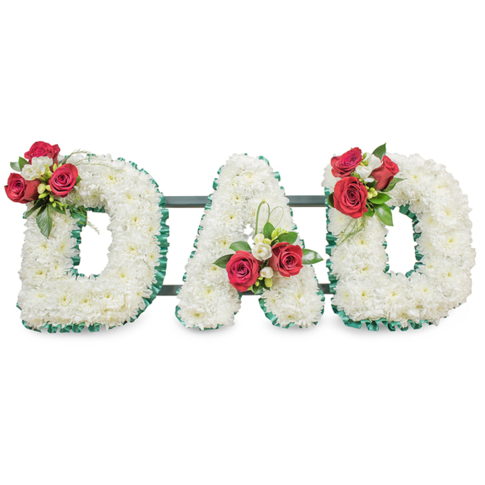 A poignant, hand-built tribute spells 'DAD' in three bold capital letters, each letter densely veneered with small, immaculate white chrysanthemum blooms so that the entire face reads as a continuous, tactile field of white. The chrysanthemum heads create a soft, almost pillowy surface, their closely set petals forming a uniform canvas for the more sculptural floral accents. Each letter is carefully outlined with an emerald green pleated ribbon, the ribbon's texture adding a crisp, architectural boundary that makes the letterforms read with clarity even from a distance. On the upper left curve of the first 'D' a concentrated spray of deep red roses clusters with stems of white freesia and glossy green foliage, the rich crimson providing an emotional focal point; the 'A' receives a corresponding cluster near the lower left diagonal, producing an upward movement in the design, and the final 'D' mirrors the first, balancing the piece. Thin dark green or black metal bars are subtly visible behind the letters, their discreet presence reinforcing the structure while allowing the blooms to remain the visual centre. Photographed against a clean, bright white backdrop under soft, diffused studio light, the composition reveals the meticulous wiring and placement of each bloom and ribbon fold - details a client might expect when arranging a service at a local church or at Highgate and nearby cemeteries. The combination of white chrysanthemums - symbols of devoted love and truth - with red roses that evoke deep affection makes this a gracious, measured tribute suitable for a father's memorial in Tufnell Park and surrounding neighbourhoods.
