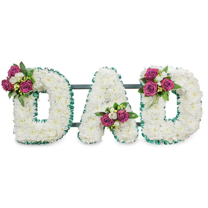 A solemn, carefully constructed sympathy tribute reading DAD, presented against a pure white backdrop so every detail is visible: each letter is densely packed with immaculate white chrysanthemums, the tiny florets forming a continuous, cloud-like texture that suggests peace and purity. The outer edges and inner cutouts of each letter are outlined in a pleated emerald-green ribbon, its ruffle lending a refined edge that separates the letters visually from the background. On each letter sits a composed spray of accent blooms - rich, magenta roses in varying stages of bloom paired with small white freesia or delicate spray flowers and deep green foliage - positioned to balance the letters visually, with clusters at the upper left of the first D, within the lower V of the A, and at the upper right of the final D. A discreet dark green or grey horizontal support bar runs behind the composition, implying stability and museum-like presentation suited to chapel displays or graveside placement. The arrangement's tactile contrasts are apparent: the chrysanthemum's soft, cushiony mass, the roses' velvety petals, and the ribbon's textured sheen. Emotionally, the piece reads as dignified and affectionate, marrying traditional funeral formality with personal colour through the magenta accents. I picture this tribute intended for an intimate service in Tufnell Park or nearby Archway, easily noticed as it stands beside a lectern or floral easel. The craftsmanship reflects the care of a local florist attuned to quiet, meaningful gestures - an arrangement designed to articulate love, remembrance and a gentle farewell for a father figure.