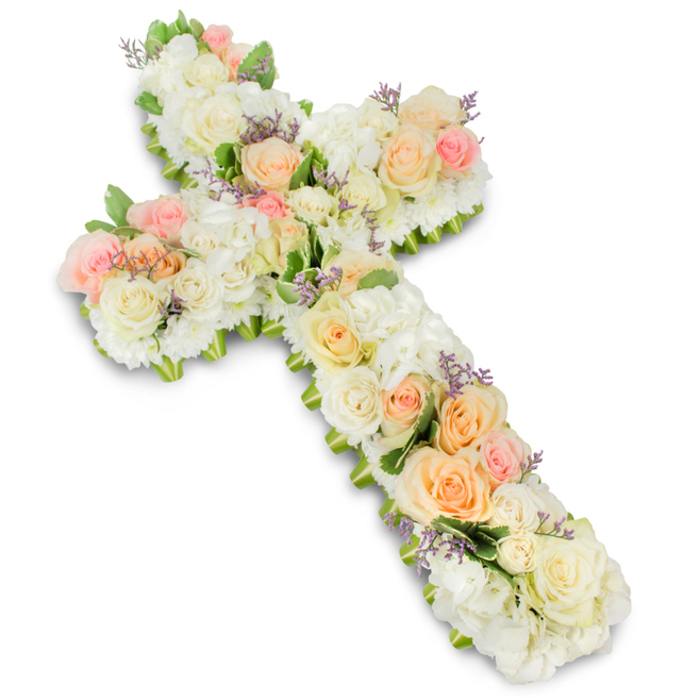 A meticulously crafted funeral flower cross dominates a bright white background, its shape instantly recognisable yet softened by a generous covering of petals in tranquil pastel tones. The cross is built entirely from fresh flowers, packed so closely that the surface appears velvety and continuous, like a soft floral tapestry. The foundation is made up of creamy white and ivory blooms-short-stemmed roses and voluminous hydrangea heads-nestled tightly together to create a plush cushion of petals. Layered over this base, clusters of roses in soft peach, honeyed apricot, and delicate blush pink are thoughtfully spaced along the vertical and horizontal arms, creating gentle focal points that draw the eye. Each pastel rose is at the height of bloom, the petals slightly ruffled at the edges, hinting at their natural fragrance. Subtle sprinkles of tiny lavender or pale purple filler flowers are scattered here and there, almost like small wildflowers tucked into a country-style design, reminiscent of the relaxed charm of local Tufnell Park gardens. Small, neat touches of soft green foliage appear mainly along the perimeter and between some blossoms, adding depth, definition, and a natural frame to the cross. The edges themselves are rounded and smooth, suggesting an experienced florist has spent time perfecting every curve and junction. A faint shadow beneath the arrangement lifts it gently from the stark white background, giving a sense of presence and weight, as though it is ready to be placed in a chapel or crematorium nearby. The overall impression is one of faith, serenity, and heartfelt condolence, capturing a respectful and loving way to say goodbye.