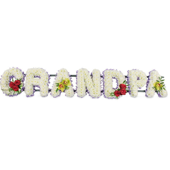 A dignified funeral flower tribute spells out GRANDPA in large, block capital letters arranged in a clean horizontal line, photographed against a plain white background that allows every detail of the floristry to be clearly seen. Each letter is generously covered with small white chrysanthemums, their rounded petals overlapping to create a thick, cushiony texture reminiscent of soft clouds drifting above Tufnell Park's tree-lined avenues. Tracing the outline of every letter is a slim border of light lavender-purple ribbon, offering a subtle halo of colour that gently frames the crisp white blooms. At the opening curve of the G, three to four deep red roses are gathered together, cradled by fresh green foliage, their rich, velvety petals adding depth and emotional intensity. The first A along the word is decorated with bright yellow-green orchids, some with delicate russet markings in the centre, providing an elegant, modern touch that contrasts beautifully with the classic chrysanthemums. In the rounded bowl of the D, another small cluster of deep red roses mirrors the arrangement in the G, creating a balanced repetition of colour. The final A is again adorned with the same yellow-green orchid blooms, bringing the design to a gentle, harmonious close. Slender, unobtrusive metal bars run behind the blooms, connecting and supporting the letters so the entire word forms one steady tribute, suitable for display at a funeral service, crematorium chapel, or graveside gathering in and around Tufnell Park. The carefully considered palette of white, red, and yellow-green flowers expresses purity, heartfelt love, and respectful remembrance for a much-loved grandfather.
