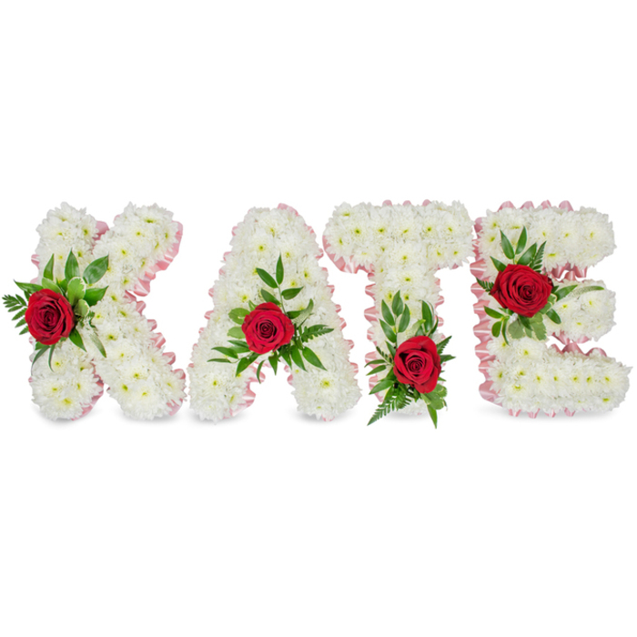 A solemn yet beautifully executed floral tribute spells KATE in substantial, three-dimensional block letters formed entirely from countless small white chrysanthemums. The chrysanthemums are packed to create a plush, cloud-like surface that reads soft to the touch and visually conveys purity and reverence; their fine petals diffuse light evenly across each letter. Along the perimeter of every letter a pale pink satin ribbon is pleated and applied as a refined border, its faintly glossy edge providing a gentle contrast to the matte softness of the blooms.
Each letter carries a single, sumptuous deep-red rose as a focal point: the K's rose is placed toward the lower portion of its left vertical stroke, the A's rose sits at the apex of its triangular peak, the T's bloom rests at the base of the left side of the horizontal crossbar, and the E's rose is positioned on the central horizontal bar. These roses are thoughtfully nestled into sprays of rich green foliage that include broad, glossy leaves and slender fern fronds, which together add layers of texture, depth, and a natural frame to the white floral forms. The arrangement is presented against a clean white background so the craftsmanship - the contrast of white chrysanthemums, pale-pink ribbon, deep red roses, and green foliage - reads with clarity and dignity.
This bespoke design is appropriate for a funeral service, memorial, or anniversary of a life dearly remembered, and reflects the careful, empathetic approach of a florist familiar with the quiet commemorations often held around Tufnell Park and nearby Dartmouth Park.