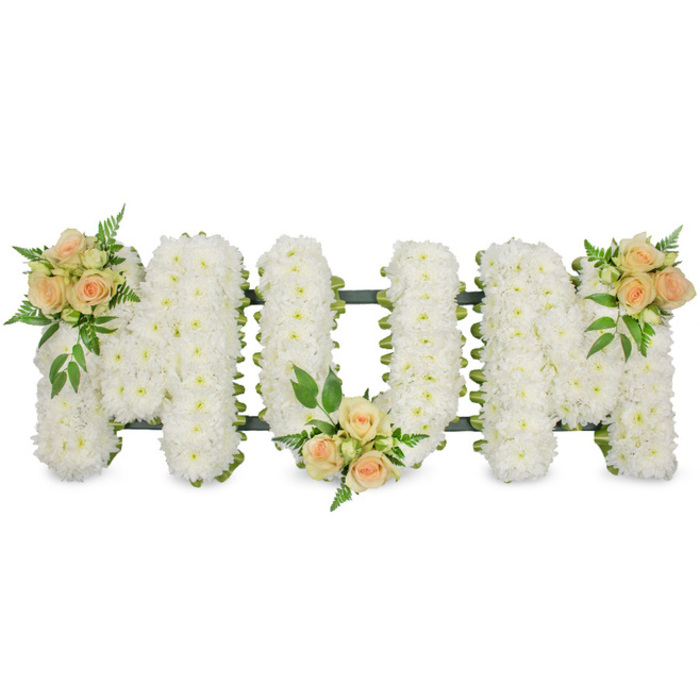 A thoughtfully composed MUM floral tribute is shown in the image, laid out horizontally yet built with strong, upright block letters that stand out crisply against a pure white background. Each of the three capital letters is meticulously formed from tightly massed white spray chrysanthemums, every small daisy-like head nestled closely beside the next to create a thick, velvety carpet of petals. The uniform white surface conveys purity and quiet reverence, while a slim dark green edge of floral ribbon and structural foliage traces around the contours of each letter, adding gentle contrast and ensuring the shapes read clearly from a distance. Across this serene base, three soft touches of colour bring warmth and individuality. At the top left arm of the first M, a cluster of peach and blush-toned roses, some fully unfurled and others in tender bud, is tucked among sprigs of glossy greenery. A second matching cluster rests at the bottom of the central U, anchoring the design, and the third mirrors the first, gracing the top right of the second M. Light fern fronds and broader, darker leaves spread delicately around the roses, giving the tribute the natural, fresh feel of flowers just prepared in a local Tufnell Park workshop. The piece is calm and dignified, designed as a loving farewell for a mother at a funeral, cremation, or memorial gathering nearby. Its combination of snowy chrysanthemums and gentle peach roses suggests innocence, cherished memories, and enduring affection, making it a touching centrepiece to accompany a final goodbye in Tufnell Park's chapels or crematoriums.