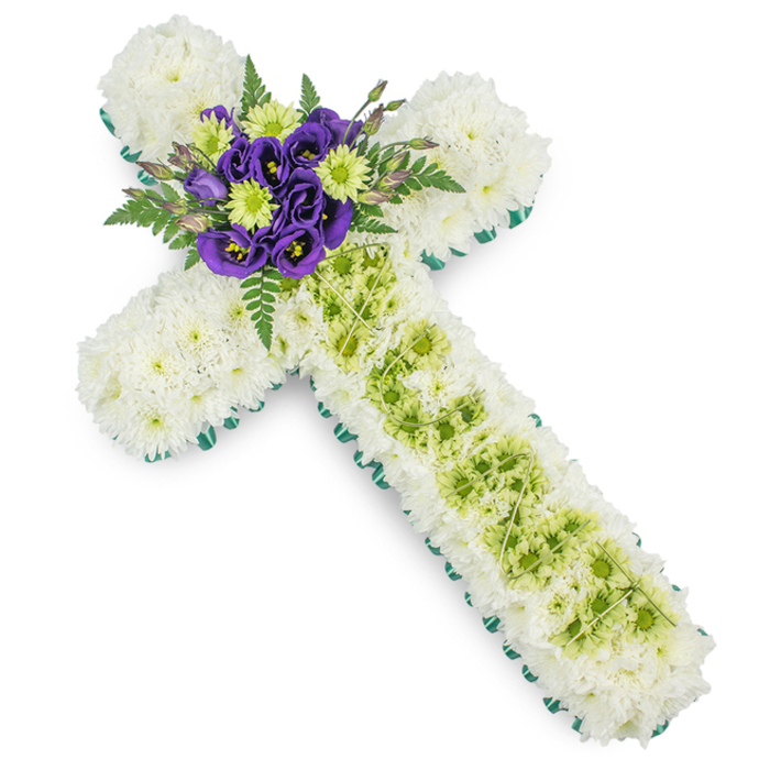 A beautifully balanced floral cross arrangement is presented against a bright, uncluttered background, allowing every detail of the design to stand out. The cross itself is generously filled with clusters of white spray chrysanthemums, arranged so closely that no gaps are visible, forming a soft, cushiony surface over the full length of the arms and stem. Their tiny, layered petals create a gentle texture that feels both pure and comforting, echoing traditional funeral flowers often chosen for services around Tufnell Park. Along the perimeter of the cross, a continuous border of crisp green-likely a satin ribbon or carefully folded foliage-runs smoothly around each curve and angle, clearly defining the Christian symbol and giving the piece a polished frame. In the centre of the vertical arm, a long panel of lime green button chrysanthemums or similar small blooms forms an eye-catching yet tasteful stripe. Fine decorative wires in a pale green tone lie over this section, arranged in soft, intersecting lines that suggest a lattice pattern, adding refinement without overwhelming the flowers. At the meeting point of the cross's arms, a striking cluster of deep purple lisianthus draws the eye, their velvety blossoms layered and slightly open, revealing darker centres. These are interspersed with fresh lime green chrysanthemums that mirror the central stripe, while dark green fern fronds and foliage splay gently behind, introducing height, movement, and a touch of wildness to the otherwise structured design. The overall composition feels calm, respectful, and dignified-a floral cross ideally suited to a Christian funeral, wake, or graveside tribute, carrying a message of peace, remembrance, and enduring love.