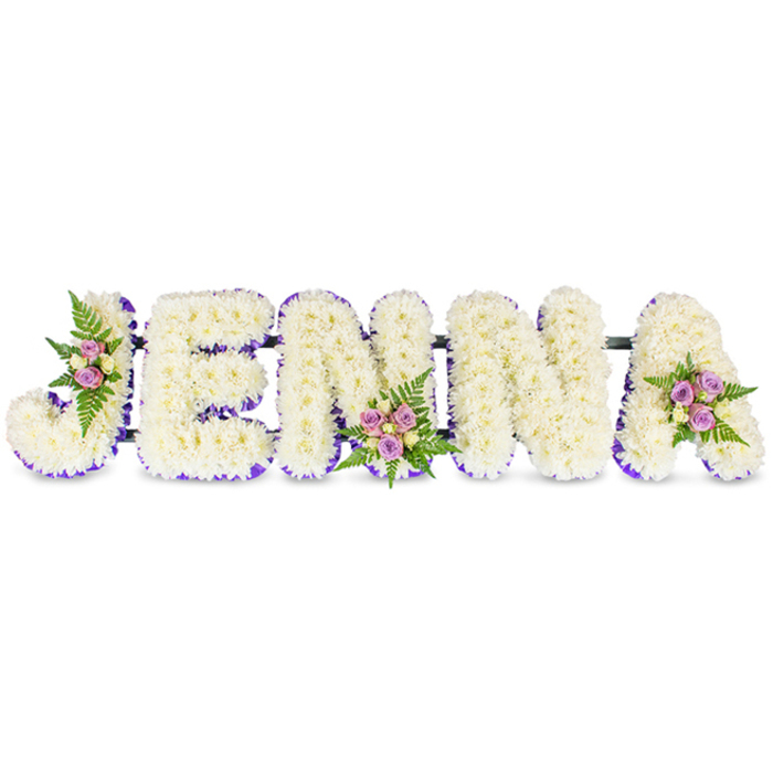 Lovingly assembled to spell the name JENNA in bold capital letters, this memorial arrangement sits against a neutral white backdrop so that every detail reads with clarity and calm. Each letter is composed of compact clusters of small, creamy white chrysanthemum-like blooms, densely set to produce a plush, cloud-like texture that invites close appreciation. A vivid purple trim-either a narrow ribbon or a tight edging of tiny lavender florets-follows the internal lines of each letter, supplying a balletic contrast that sharpens the form without disturbing the arrangement's solemn grace. Three ornamental clusters punctuate the design: a soft gathering of blush and lilac spray roses on the upper left of the J, a midline cluster on the first N that includes pale yellow-cream roses, and a final spray on the A accented with feathery fern. These touches add small pockets of colour and the fresh, green scent of foliage to the otherwise serene white composition.
The letters are discreetly linked by thin, dark structural bars to keep the tribute cohesive for placement on an easel or in a funeral setting. The overall atmosphere is one of respectful remembrance-textural, fragrant and carefully balanced-suitable for memorial services in Tufnell Park, local churches and funeral homes around Junction Road and Kentish Town. It reads as an intimate, bespoke gesture: a name held in flowers, crafted to give comfort and a tangible focus for farewell.