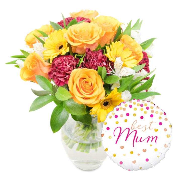 An artfully arranged bouquet rests in a clear glass vase, shown against a pure white background, with a bright, personalised foil balloon positioned at the lower right - a classic Mother's Day pairing familiar to our Tufnell Park customers. The bouquet is a warm, harmonious mix: several large orange-peach roses with velvety, spiralled petals take centre stage, while sunny yellow gerbera daisies with dark brown centres fling rays of cheer outward. Rich burgundy carnations provide luxurious, ruffled volume and a tactile, plush contrast to the smoother roses. Fine clusters of white alstroemeria, each petal lightly freckled, breathe an elegant, delicate air through the composition. A generous cloud of glossy green foliage - wide leaves and slimmer sprigs - frames the blooms, adding weight, structure, and the crisp, green scent of freshly cut stems visible through the transparent vase. The round white Mylar balloon overlaps the base of the vase and lower stems, sprinkled with gold and fuchsia dots and small heart motifs; across its centre, a flowing fuchsia script reads best Mum, a warm message that immediately personalises the gift. Presented in soft, neutral lighting that highlights colour saturation and texture without glare, the arrangement feels like something crafted by a local hand for a neighbour - perfect for celebrating a birthday, Mother's Day, or an afternoon tea on Fortess Road. Flowers Tufnell Park often pairs this style of bouquet with a message balloon for a heartfelt, neighbourhood-ready present.