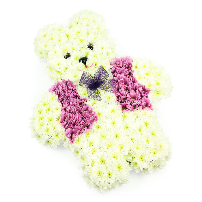 This image shows a beautifully detailed teddy bear-shaped floral tribute, the sort of thoughtful design a Tufnell Park family might choose when words are hard to find. The bear's body is entirely covered in tightly placed white and pale ivory chrysanthemums, their petals overlapping in soft layers that resemble plush fabric. From the rounded head with its sweet, lifted ears to the solid, reassuring legs at the base, every shape is clearly defined, giving the impression of a beloved soft toy recreated in flowers. Two small, dark eyes sit neatly above a tiny triangular black nose, lending the face an expression that is gentle and protective rather than sad. A suggestion of a smile is hinted at by the careful placement of petals around the muzzle, evoking warmth and reassurance for those attending a funeral or remembrance service near Tufnell Park Fields. Across the front of the bear, rich magenta and deep pink blooms form a floral waistcoat, arranged in two symmetrical panels that open slightly at the centre. Just where a collar might sit, a neat bow of fine, dark purple net is tied, the delicate mesh adding both texture and a touch of elegance, as if the bear is dressed with care for a special farewell. The pure white background allows the colours and details to stand out without distraction, much like the quiet stillness of a service room off Junction Road. This floral teddy is perfect as a tribute for a child, a baby memorial, or anyone whose memory is wrapped in innocence and affection, conveying comfort, tenderness, and a sense of being lovingly held.