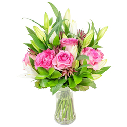 A carefully composed bouquet of deep pink roses and poised white lily buds, arranged in a transparent glass vase, evokes warmth and the quiet joy of receiving fresh flowers at home. The roses are the visual anchor: several generous blooms have unfurled into full, velvety rosettes with shades ranging from soft blush near the heart to a richer fuchsia on their outer petals, each petal catching a soft sheen. Interlaced between them are tall, elegant lily buds - many closed, the promise of trumpet-shaped white flowers, a few beginning to open and reveal their clean, satiny inner petals and the pale green of their throats. A lush assortment of greenery provides volume and contrast: broad, glossy leaves offer structure while finer, lighter-green sprigs create breathing space and a gently wild texture. Scattered darker burgundy or reddish-brown accents add sophistication and visual depth, grounding the palette. The clear vase, with a slightly tapered base and flared rim, contains pristine water that showcases the arranged stems and the careful trimming typical of an experienced florist. The lighting is bright and unobtrusive, suggesting a crisp morning in Tufnell Park near Junction Road where the flowers might arrive by hand, filling a kitchen with a soft, floral scent and a sense of celebration. This bouquet reads as both a thoughtful gift and a calming presence for everyday life - suited to birthdays, thank-yous, or simply to lift a Hampstead-bound commuter's spirits after a damp walk.