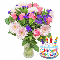 Bathed in gentle morning light, this sumptuous bouquet feels both joyful and quietly elegant-a birthday gift that reads like a promise. At its heart are soft pink roses, petals unfurling in delicate spirals from palest blush to a deeper rose tone, each bloom poised and fragrant in a way that suggests they were cut at dawn. Intertwined among them are generous pink Gerbera daisies, their large, open faces like smiling suns with pale, butter-coloured centres that catch the eye. Clusters of vivid purple statice thread through the arrangement, their crisp, papery texture creating depth and a lively colour counterpoint to the soft pinks. Glossy, varied green foliage provides a lush backdrop, the leaves cradling the flowers and giving the bouquet a full, garden-picked silhouette. The flowers rest in a clear glass vase with a slightly wider base; you can see the stems and water below, a reassuring sign of freshness. A whimsical 'Happy Birthday' motif completes the scene, suggested by a nearby foil cake balloon with blue piping, colourful sprinkles and multi-coloured lettering-details that make the bouquet an unmistakable celebration. The scent is described as faint and sweet, not overpowering, the kind of fragrance that evokes a Tufnell Park morning walk past community gardens or the green expanse of nearby Hampstead Heath. This is the sort of arrangement our team at Flowers Tufnell Park would carefully prepare for a local birthday delivery: considered, bright and quietly joyful, designed to bring a smile whether it's picked up on Junction Road or dropped at a home near Dartmouth Park.