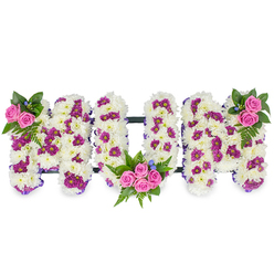 Arranged with the quiet care of a neighbourhood florist, this three-dimensional MUM tribute rests against a clean white backdrop so each letter is immediately legible and dignified. The primary construction is a dense mattress of ivory-white chrysanthemums, their soft, clustered petals forming a tactile, almost cloud-like surface that reads as gentle and consoling. Scattered through the white are small groupings of deep purple and magenta spray chrysanthemums, introducing depth and a tasteful contrast that lifts the composition without overpowering it. Small clusters of vivid pink spray roses punctuate the piece: a modest pair sits at the upper left edge of the first M, a more abundant bouquet of four to five roses nestles into the lower sweep of the U, and a matching cluster adorns the upper right of the final M. Rich fern fronds and dark green foliage cradle each rose group, their varied textures accentuating the softness of the chrysanthemums, while tiny blue accent flowers offer a discreet cool counterpoint. A thin dark bar links the letters, holding the ensemble together with unobtrusive structure. The effect is both traditional and personal - a tribute that speaks of enduring love and careful workmanship. As someone who prepares tributes for families around Tufnell Park, from Fortess Road to Dartmouth Park, I imagine this placed beside a photograph or near a service book, the subtle scent of roses and chrysanthemums filling the space. Flowers Tufnell Park can recreate this arrangement for memorials or wakes, delivering a composition designed to comfort and honour with composed, expert hands.
