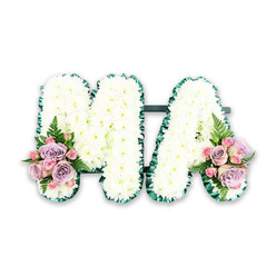 This image shows an elegant floral funeral tribute carefully shaped into the word MA, designed as a personalised farewell for a much-loved mother or Mama. The two capital letters sit side by side on a clean white backdrop, making every petal and contour easy to distinguish. Each letter is densely filled with flawless white chrysanthemums, placed so closely that no gaps of foam or backing can be seen, creating the impression of soft cushions of snow or freshly fallen blossom. Around the outside edge of the M and A runs a slim yet distinct border of dark green, likely folded satin ribbon or finely trimmed foliage, expertly worked to give a sculpted, ruffled finish. This rich green frame sets off the crisp white blooms and adds a sense of structure to the design. At the lower left foot of the M and the lower right side of the A, clusters of pastel flowers bring gentle colour: blush-pink roses, lilac or lavender roses, and tiny spray roses, all with velvety petals and a romantic, layered look. Delicate fern fronds and fresh green leaves emerge between the blooms, echoing the greenery of nearby Tufnell Park playing fields or the tree-lined streets off Fortess Road. The tribute feels serene and heartfelt, suggesting the soft fragrance of roses mingling with the clean scent of chrysanthemums. It evokes the quiet moment when family and friends gather in a local chapel or crematorium, the MA letters lying proudly among other tributes, an expression of enduring love created with the care and precision of a seasoned Tufnell Park florist.