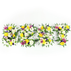 Viewed head-on, this elegant tribute spells the word 'BEST' in four substantial letters, each letter densely packed with a garden's worth of fresh blooms and rich greenery. The dominant palette is sunlit yellow and pristine white: buttery yellow roses and bright yellow gerberas bring warmth and cheer, while large, chrysanthemum-like white blooms lend a soft, timeless purity. Interspersed among them are small clusters of mauve and purple lisianthus or petite chrysanthemums that add calm depth, and vivid fuchsia spray roses or carnations that offer moments of joyful colour. Light green and white filler flowers ripple between the larger blooms, creating gentle texture and a sense of layered volume. Dark green fern fronds are tucked around the perimeter of each letter, their feathery tips softening the letter shapes and providing a verdant frame against the clean white background. You can also spot a subtle metal or dark-green framework that supports the shapes, visible through a few narrow gaps-an understated reminder of the careful construction required to make such large lettering sing. The lighting is even and bright, showcasing freshness and the delicate interplay of petal surfaces. As a local florist with hands-on experience in Tufnell Park, I picture this piece at a remembrance service near Junction Road or placed beside a funeral cortege passing Fortess Road: it reads as a heartfelt memorial, a phrase of farewell and affection, remembering someone as 'the best' with the quiet dignity that flowers can give.