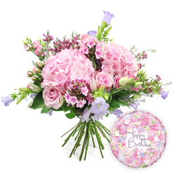 A luxurious birthday bouquet is arranged in the centre of a pure white backdrop, every petal and stem carefully placed to feel both abundant and airy. The composition is dominated by rounded heads of pale blush pink hydrangea, their petals overlapping in dense, pillowy clusters that give the design generous volume and a soft, romantic texture. Nestled among them, classic soft pink roses appear at different stages of opening: some blossoms are wide and open, revealing their intricate spirals, while others remain in cupped bud form, like promises of tomorrow's beauty. Between these larger blooms, dainty sprays of brighter fuchsia or magenta waxflowers weave in and out, their tiny star-shaped flowers adding both colour contrast and a fine, almost lace-like detail. Rising elegantly through the pinks, slender stems of campanula show off bell-shaped flowers in lavender and cool lilac hues, providing a subtle shift into purple that keeps the eye moving around the arrangement. The entire bouquet is wrapped in a halo of fresh greenery, from elongated, pointed leaves to softer, rounded foliage, creating a natural frame that enhances the pastel tones and gives the sense of something freshly gathered from a North London garden. The cut stems are clearly visible at the base, neatly bound as a hand-tied bouquet ready to drop into a vase the moment it arrives in a home near Tufnell Park station or along Brecknock Road. To the lower right, a glossy round foil balloon adds a joyful finishing note. Its surface shimmers with a delicate floral pattern in coordinating shades of pink, cream, and lavender, and across the centre, the words "Happy Birthday" are written in a flowing purple script that feels personal and celebratory. The overall effect is that of a carefully curated birthday gift set, perfectly suited to surprise someone in Tufnell Park with a burst of colour, fragrance, and heartfelt sentiment.