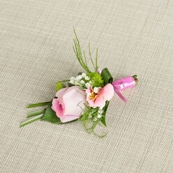 As if conjured from an early Tufnell Park morning, this lovingly constructed buttonhole weaves together gentle blush and lively green, embodying the heartfelt spirit of local celebrations. At its core, a tightly furled pink rose stands shy yet promising, its pale outer petals embracing a richer, deep pink within. Framing the rose is an open alstroemeria bloom, tinged with luminous peach and brushed with fine, dark markings-an echo of wildflowers along the Parkland Walk. Plumes of white baby's breath add a weightless, airy counterpoint, while plump, vibrant green miniature pompoms nestle amid glossy leaves, echoing springtime freshness along Fortess Road. Slender spikes of grass and wispy, fern-like greens reach upward, establishing an organic movement that contrasts artfully with the dark folded leaves forming the arrangement's base. Tied with a glossy fuchsia ribbon, the stems curve gently as if reading the contours of the handwoven, ecru linen beneath. The boutonniere radiates soft celebration-its satin finish and fragrant petals tailor-made for a wedding, prom, or life's quieter milestones. Worn close to the heart, it imparts a sense of calm confidence and sincerity, as if carrying an emblem of Tufnell Park's familiar warmth. This arrangement is a testament to the artistry and care found in local floral design, crafted for those who cherish moments of tenderness and festivity in their North London community.