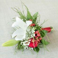 Poised gracefully upon a backdrop of soft, oatmeal-toned linen reminiscent of a well-loved tablecloth, this small yet striking bouquet brings a hint of Tufnell Park's lively spirit into the floral world. At its heart lies a fully unfurled white lily, petals broad and serene, each marked with delicate rust-hued freckles and a sunlit center of yellow anthers. Nearby, a deep red rose spirals inward with lush velvet petals, their warmth hinting at both love stories and neighborhood strolls through Tufnell Park's green spaces. Interlaced among the feature blooms, dainty baby's breath forms a light, whispering veil, while clusters of gleaming red berries evoke the cheerful bustle of local seasonal markets. To the side, a green lily bud stretches forward, invoking both promise and anticipation. A rich assortment of greenery-fine ferns, robust dark leaves-frames the blooms and provides dimension, all expertly tied with a lustrous scarlet ribbon. Crafted by local hands, this bouquet embodies artistry and tradition, perfect for Tufnell Park weddings, anniversaries, or heartfelt moments. Soft natural light brings every shade to life, inviting the senses to linger on the gentle fragrance and the skillful textures of blooms gathered by Flowers Tufnell Park-a reflection of the area's authentic floral heritage.