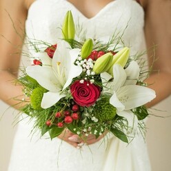 Artistry and sentiment intertwine gracefully in this elegant wedding bouquet, freshly gathered by an expert florist in the heart of Tufnell Park. Set against the soft white folds of a bride's classic gown-her hands resting gently at the bouquet's base-the arrangement radiates both purity and passion. Luminous white oriental lilies, with their golden stamens dusted gently across wide, silky petals, unfold alongside velvety, deep crimson roses that evoke enduring love, much like the community spirit found on Dartmouth Park Hill. Emerging green lily buds peek from between blooms, brimming with anticipation and youthful vibrance. Wispy baby's breath floats in delicate clouds, softening the composition and weaving a sense of London's ever-present breeze through the flowers. Here and there, juicy red hypericum berries glisten boldly, adding movement and a celebratory spark balanced by clusters of unique, moss-green button flowers and sprigs of trailing foliage. The bouquet's wholesome, textured foundation is reminiscent of the wild green spaces around Tufnell Park station, offering a nod to the area's leafy vibrancy. Every bloom and stem has been thoughtfully selected-tactile, fresh, and alive-creating a bouquet ready to carry a bride's dreams down the aisle. This is more than a floral accent; it's a heartfelt tribute to new beginnings in North London, rich with colors, scents, and memories ready to blossom anew.
