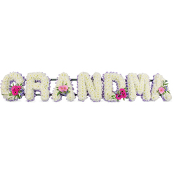 This image shows a thoughtful funeral flower display where the word "GRANDMA" is formed in bold, upright letters, each one densely covered in snow-white chrysanthemums so tightly packed they resemble soft cushions or freshly fallen petals. The chrysanthemums create a smooth, uniform texture, their tiny, ruffled petals catching the studio light and giving the tribute a luminous, comforting glow. Tracing the outline of every letter is a fine lilac ribbon, folded neatly to hug the curves and corners, providing a subtle pastel border that adds poise without overwhelming the simple beauty of the white blooms. Nestled into the arrangement at three points-the opening "G", the central "A", and the ending "A"-are compact sprays of pink gerberas and delicate pink roses. The gerberas bring a cheerful daisy-like openness, while the roses add a softer, romantic note; both are interwoven with glossy green foliage that introduces depth and natural movement. The design feels as if it has been assembled by an experienced local florist who understands the gentle, understated style favoured by many Tufnell Park families, perhaps preparing this piece for a quiet service near the station or by Tufnell Park Playing Fields. Though the photograph cannot convey scent, you can almost sense the fresh, slightly herbal fragrance of the greenery blending with the mild, clean aroma of the chrysanthemums. The overall mood of the piece is serene and reflective, a floral tribute that holds space for shared stories, warm kitchen conversations, and the lasting presence of a cherished grandmother.