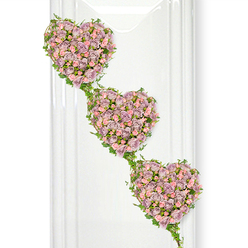 Three intertwined hearts made entirely of roses descend like a tender garland of memories, creating a touching funeral tribute that feels at once delicate and deeply grounded in love. Each heart is wrapped in a dense tapestry of soft lavender and muted mauve roses, interspersed with smaller clusters of pastel pink spray roses, their petals layered in tiny ruffles that suggest both fragility and strength. From top to bottom, the hearts are staggered in a diagonal cascade, so the eye naturally follows their line as though tracing the journey of a shared life or a family's generations. Around every heart, a finely worked border of trailing green ivy curls and winds, its glossy leaves overlapping the floral edges and stretching between each shape like living ribbons of connection. The greenery introduces a gentle woodland freshness, reminiscent of quiet walks through the tree-lined streets and hidden corners around Tufnell Park, grounding the design in something calm and familiar. The arrangement is photographed against a pure white background, with soft, diffused light that highlights the subtle variations in petal colour-from dusty lilac to shell pink-while faint vertical reflections along one side suggest a contemporary interior or glass-panelled chapel. There is no harsh contrast; instead, the entire piece feels serene and contemplative, ideal for expressing sympathy and a lasting bond. This triple-heart composition would be chosen by someone wishing to honour a partner, parent, or close relative with a symbol of continuous, unwavering affection, delivered to a Tufnell Park funeral home, church, or family address as a gentle, beautifully crafted farewell.