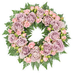 A serene, circular floral wreath is shown laid flat on a clean white surface, its symmetrical ring form appearing almost like a soft floral halo. The arrangement is densely woven with roses in gentle, understated shades, giving the impression of a calm, thoughtful tribute designed for a farewell gathering in Tufnell Park. Large, fully open roses in dusty lavender, antique mauve, and greyish-purple tones anchor the design, each bloom revealing layers of delicately ruffled petals spiralling inward to a shaded centre. Between these statement roses, clusters of smaller, pastel pink spray roses thread through the circle, some still close-bud, others just opening, providing a mix of textures that feels both tender and alive, like moments of a shared life recalled in fragments.   

Beneath and around the flowers, a lush foundation of deep green fern fronds forms a continuous, textured border. The foliage, possibly leatherleaf or sword fern, fans outward with fine, serrated leaves that cradle the roses and create a natural frame, adding depth and structure to the wreath. Tiny accents of darker greenery and discreet buds are tucked among the blooms, quietly enriching the composition without disturbing its harmony. The white background and soft, even lighting make every colour and contour stand out clearly: the soothing purples and pinks, the velvety petals, and the fresh, cool greens. This wreath feels especially fitting as a sympathy flower arrangement for a funeral or crematorium service near Tufnell Park or along Junction Road, where families gather in remembrance. Its gentle palette and thoughtfully balanced design express condolences, respect, and peace, offering a comforting floral presence that surrounds grief with grace and enduring affection.