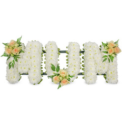 The image shows a graceful funeral flower tribute spelling out MUM in large, upright capital letters, presented against a bright white backdrop that makes every detail stand out. Each letter is completely covered in tightly arranged, pristine white spray chrysanthemums, their countless tiny blooms forming a smooth, cushion-like surface that looks soft to the touch and quietly luminous. A neat framework of dark green ribbon and support foliage peeks out just around the edges and through some inner lines, delicately outlining the shape of each letter and hinting at the careful craftsmanship behind the design. To soften the crisp white base, three gentle accents of colour run across the tribute. On the top left corner of the first M, a cluster of warm peach and blush pink roses, some opening, some still in bud, nestles among fresh green leaves. A second cluster sits at the lower curve of the U, while the third rests on the top right of the final M, providing a balanced, almost story-like progression from left to right. Fine fern fronds and darker, broader leaves fan out from the roses, adding texture and depth similar to the greenery found in local Tufnell Park terraces and pockets of parkland. The arrangement feels peaceful and deeply respectful, evoking the tenderness and strength of a mother's love. Crafted as a bespoke memorial piece, it would sit beautifully beside the coffin during a funeral service in or around Tufnell Park, offering a heartfelt, visually simple yet emotionally rich message of love, remembrance, and farewell from her family.