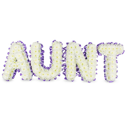 Carefully arranged by a local hand, this floral letter tribute spells AUNT in bold, capital forms crafted entirely from pristine white spray chrysanthemums. The chrysanthemums are densely set, their small, ruffled petals forming a soft, cloudlike texture across each letter; occasional pale yellow centres peek through, adding a touch of warmth that prevents the design from feeling austere. Each letter is edged with a rich purple satin ribbon that has been gently pleated to produce a scalloped, tactile border; the ribbon's lustre contrasts beautifully with the velvety matte of the petals and frames the wording with quiet elegance. Against a clean white background the letters appear almost suspended, their three-dimensional quality reinforced by delicate grey shadows that reveal the contours of the supporting frames. There is a restrained, fresh scent-green, clean, and slightly floral-that speaks to the chrysanthemums' recent conditioning and the meticulous care of the maker. Intended as a personal, bespoke memorial, this tribute communicates loving remembrance and gentle dignity: the white for purity and the purple for respect. As Flowers Tufnell Park, we know these designs often sit beside a service order or family photograph at local venues near Tufnell Park tube, Junction Road chapels, or small church gatherings in Upper Holloway. The overall effect is a composed, comforting farewell that honours an aunt's place in family stories while offering consolation to those who gather.