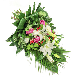 Crafted with the care and skill that define Tufnell Park's local florists, this distinguished, cascading floral arrangement offers a tapestry of colour and meaning set against a stark white canvas. White lilies-some open, unfurling star-like petals, others just beginning to reveal their promise-anchor the composition with their calm purity and subtle, sweet aroma. Between lilies, clusters of rich fuchsia and blush-pink roses emerge, their velvet petals layered closely in a gentle embrace, carrying warmth and memory that feels at home along leafy Tufnell Park avenues. Whites continue in the gentle ruffles of petite carnations, filling every gap with softness, while vivid green button chrysanthemums punctuate the design with playful orbs that shimmer under natural light-echoes of nearby local green spaces. Wisps of bold red hypericum berries surprise the eye, their small, shiny forms adding rich contrast to the arrangement's overall palette. A profusion of foliage wraps the flowers, with glossy broad leaves and lighter green fronds creating both rhythm and structure-some leaves meticulously folded to guide the gaze, others left trailing with organic grace. The result is a bouquet that whispers of heartfelt tribute and gentle solace, ideal for commemorating a cherished life, be it in a quiet chapel by Tufnell Park or a gathering along Lady Somerset Road. Every stem and bloom, freshly sourced, reflects a sense of community and care, inviting contemplation, remembrance, and peaceful farewell.
