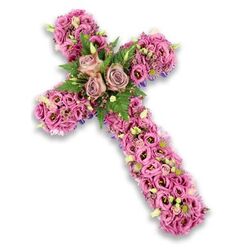 This image presents a meticulously crafted floral cross, photographed against a clean white background so that every nuance of colour and texture stands clear. The entire cross is carpeted with flowers, dominated by gentle pinks, mauves, and lilac-purples that blend together like a soft evening sky over Tufnell Park Fields. At the centre, three large roses in a delicate dusty rose tone are fully unfurled, their overlapping petals forming a calm focal point that draws the eye inward, much like a place of quiet reflection in a familiar local church. Surrounding them, fronds of fresh green fern and glossy foliage provide a natural, woodland contrast to the pastel blooms, suggesting new life and hope. The vertical and horizontal arms of the cross are packed tightly with trumpet-shaped lisianthus flowers in various pink and mauve shades, some with darker centres that add subtle drama and depth. Interlaced among them are tiny sprigs of pink and purple filler flowers, clusters of small white blossoms, and emerging light green buds, each detail contributing to a layered, almost woven effect. A glimpse of deeper purple ribbon or structural fabric edges the cross in places, giving definition to the contours without overpowering the blossoms. The flowers appear fresh and lovingly placed, as if arranged in the early morning before a funeral or memorial service on a quiet Tufnell Park side street. This floral cross reads as an expression of sympathy and remembrance, designed to bring gentle comfort and spiritual reassurance to grieving families, whether displayed beside a coffin, at a graveside, or near the front of a modest local chapel.