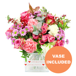 A generous, garden-fresh bouquet rises proudly from a modern, square glass vase, captured against a clean white backdrop so the colours glow with clarity. The main impression is pink: lush, full-headed roses in deep fuchsia and soft pastel shades open their layered petals beside frilly carnations in coral, salmon, and romantic blush-pink. Creamy white carnations bring a gentle calm to the mix, allowing the brighter tones to sing without overwhelming the eye. Scattered throughout, small daisy-like chrysanthemums in lavender and purple, each with a luminous chartreuse-green centre, lend a playful energy and a slightly wild, meadow-like charm that would feel just as at home on a table near Tufnell Park Underground as in a living room off Brecknock Road. The foliage is thoughtfully composed, with rounded eucalyptus in silvery green, darker glossy leaves, and slight hints of reddish-brown stems that echo the warmth of late-afternoon light over nearby Hampstead Heath. The bouquet is arranged in a clear glass vase with softly rounded corners, wrapped around its base by a crisp white band decorated with repeating red hearts and the phrase all my love, making the romantic intention unmistakable without being overly formal. At the lower right of the image, a bold orange circle announces VASE INCLUDED in white uppercase letters, emphasising that the flowers arrive as a complete, ready-to-enjoy gift. The composition feels caring and personal, the kind of thoughtfully arranged floral gift a local Tufnell Park florist might send for anniversaries, birthdays, Mother's Day, or simply to say I'm thinking of you to someone nearby in Kentish Town or Archway.