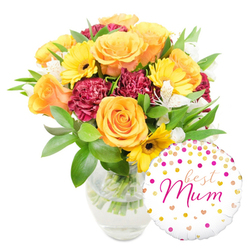 A lovingly composed floral gift sits against a clean white backdrop, the bouquet occupying the centre-left and a glossy white balloon playfully nesting at the bottom right, slightly overlapping the vase. Peach-orange and bright yellow roses form the heart of the design, their layered petals curling softly outward like small suns and giving off a gentle, sweet perfume that hints of summer gardens. Sunny yellow gerbera daisies punctuate the arrangement with cheerful faces and dark, tender centres, while deep maroon carnations supply velvety texture and depth with their densely crimped petals. Sprigs of white alstroemeria - slender, speckled and delicate - weave through the bolder blooms, adding a light, airy contrast and a refined silhouette. The greenery is abundant: glossy, broad leaves and finer fern-like stems that cushion each bloom and add a fresh, slightly green scent when you hover close. The round foil balloon is white with scattered gold and hot-pink confetti dots and tiny hearts, and the graceful hot-pink hand-lettered message best Mum sits centrally, unmistakably personal. The clear glass vase shows clean water and tidy stems, a visual promise of freshness and care. The overall mood is celebratory but intimate, a bouquet that feels handcrafted in a neighbourhood workshop and designed to make a mother smile on mornings full of light and soft conversation.