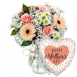 A tender Mother's Day scene unfolds against a spotless white backdrop, where colour, texture and sentiment are allowed to speak clearly, much like a calm spring morning in Tufnell Park. In the centre stands a clear glass vase, simple and slightly rounded, its neck cinched with a slim tie of natural twine that suggests a bouquet thoughtfully finished by hand. Rising from the vase is a lush mix of fresh flowers: soft peach and blush-pink roses with silky, spiralled petals sit alongside generous peach-orange gerbera daisies, their open faces and dark, almost black centres radiating easy cheer. Interlaced among these statement blooms are airy sprays of white baby's breath that soften the whole design, and neat little white chrysanthemums whose pale green cores add a gentle spark of brightness. Glossy green foliage peeks through from behind and between the flowers, framing them with natural movement and giving the arrangement a just-picked feel, as if it could have come from a local garden off Brecknock Road. Just visible behind the bouquet is a small white card, its colourful lettering slightly obscured but clearly meant as a heartfelt Mother's Day message. Anchored at the base and leaning towards the flowers is a large, heart-shaped foil balloon. The balloon is crisp white and scattered with metallic gold and silver polka dots that shimmer, while at its centre a soft peach heart holds the phrase "HAPPY Mother's DAY" in bold black lettering, with "Mother's" written in graceful, flowing script. The overall impression is of a bright, affectionate gift combination - flowers and balloon together expressing gratitude, warmth and celebration, ready to be delivered to a loved mum anywhere around Tufnell Park and the neighbouring streets.