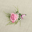On a pale, sand-toned fabric that suggests handwoven linen, a carefully crafted boutonniere lies ready to be pinned to a lapel, its simplicity revealing the loving detail of expert floristry. At its centre, a single pink rose draws the eye, angled slightly across the frame as if caught in a quiet pause before the ceremony begins. The petals show a gentle ombré of colour, with outer edges brushed in rich magenta and inner whorls softened to blush and baby pink, giving the flower a velvety, almost luminous quality. Surrounding this focal bloom, clouds of white baby's breath soften the outline, each miniature flower adding lightness, like distant wedding bells echoing across the streets of Tufnell Park and up towards Archway. Wispy, grass-like fronds extend delicately behind the rose, their lines fine and expressive, while a single, more substantial green leaf curves around the base, forming a natural cradle. Tiny droplets of water rest on its surface, capturing flecks of light and suggesting freshly conditioned stems, just prepared in a local studio off Tufnell Park Road. The stems are tightly wrapped in a satin ribbon the colour of pale pink silk, its texture smooth and slightly reflective. Near the base, a narrower strand of darker, magenta-pink ribbon is tied in a small, neat bow, adding a tailored finish. The overall composition feels calm, romantic, and composed, perfect for a groom walking from Tufnell Park station to a nearby ceremony, or for anyone wanting a classic rose accent for a formal event in North London.