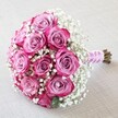 Delicately poised on a textured, light fabric that channels the artisanal heart of Tufnell Park, this enchanting bouquet is a masterclass in romance and classic floral design. About a dozen pink roses, ranging from muted mauve-lavender in the heart to bold magenta at the petal tips, are expertly clustered into a rounded, opulent shape. Lovingly woven among the roses, clusters of pure white baby's breath create a dreamy, cloud-like effect-softening the arrangement's outlines and enhancing its sense of freshness and volume. The natural stems are trimmed and tightly bound in a lustrous, blush-pink ribbon, which is elegantly spiraled with tiny, iridescent pearls; the thoughtful detail of the wrap is perfect for holding during ceremonies along Campdale Road or celebrations in local Tufnell Park venues. A few green-brown stem ends peek out from beneath the ribbon, confirming the flowers' just-cut vitality. The scene is cast in balanced, diffused light, which gently highlights the plush petals, shimmery ribbon, and the delicate lacework of Gypsophila without casting harsh shadows. The overall presentation is of tranquil beauty and enduring love-a bouquet that would feel at home in a wedding, anniversary, or as a heartfelt token of affection for anyone lucky enough to call Tufnell Park home.