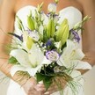 The spirit of a Tufnell Park wedding morning lingers in this radiant bridal bouquet, captured just as gentle sunlight filters through Victorian windows. Broad white Oriental lilies unfurl with luminous poise, their petals dusted with delicate speckles and cradling sunlit stamens, while tightly furled buds await their turn to bloom. Cool lavender-edged lisianthus-ruffled and slightly wild-dance against the veil of soft white baby's breath, conjuring the playful charm of local meadows. Deep purple veronica provides a pulse of colour, while abundant greens-broad leaves and feathery ferns-spill gracefully, echoing the lushness of Waterlow Park or local gardens. The entire bouquet is held thoughtfully in the bride's glowing hands, nails dressed in a hint of pale polish, the dress softly blurred in the background. Fragrance and freshness intermingle, a scent both grounding and ethereal, resonant with the promise and hope of a wedding day in Tufnell Park. Each detail, from flower to foliage, reflects the artistry and joyful anticipation that define the area's bespoke floral designs-created for unique love stories to bloom in north London.