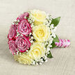 A round, hand-tied bouquet is laid carefully on a neutral, woven fabric that looks like fine linen or hessian in a warm oatmeal tone, the perfect backdrop for its romantic colours. The arrangement is split into two harmonious halves that meet seamlessly at the centre: one side is filled with bold fuchsia and magenta-pink roses, each bloom fully opened, petals layered like satin ruffles; the other side is composed of gentle, creamy yellow roses, glowing softly and balancing the vibrancy of the pinks. Between these roses, delicate sprays of white baby's breath drift like a fine mist, light and feathery, giving the bouquet a dreamy, almost ethereal atmosphere. Subtle, glossy green leaves peep from behind the blooms, tracing the outer edge, adding depth and echoing the fresh greenery you might notice in nearby Dartmouth Park or on a quiet side street off Tufnell Park Road. The stems are trimmed and bound tightly, creating a smooth handle that feels comfortable in the hand. This handle is wrapped in a shimmering pink satin ribbon, slightly reflective, lending a polished, tailored finish. Coiled around the ribbon is a dainty strand of white pearls, evenly spaced in a gentle spiral, suggesting bridal jewellery and adding a note of quiet luxury that would look perfectly at home in a Tufnell Park wedding or vow renewal. The bouquet feels fragrant and full of life, ideal for walking down the aisle, posing for photos in local gardens, or surprising someone special with a romantic, hand-delivered gift that speaks of devotion and care.
