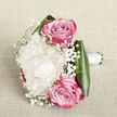 A delicately composed bouquet lies on a pale, linen-like fabric, photographed from above as though resting on a carefully laid table in a Tufnell Park flat before the wedding car arrives. At its centre, a single large peony in a soft, creamy white hue opens in layered ruffles, each petal slightly curled and gently shadowed, giving the bloom a plush, cloud-soft appearance. Nestled close to this focal peony, two pink roses draw the eye, one positioned just above and one slightly below, their petals spiralling tightly at the core and gradually unfurling into a richer magenta tone at the edges. These roses introduce a sense of passion and tenderness that feels at home in the quiet streets off Tufnell Park Road. Throughout the bouquet, wisps of baby's breath weave in and out, tiny white blossoms suspended on fine, branching stems that add an airy, lace-like texture and soften the transitions between the larger flowers. Around the base, polished dark green leaves curve neatly to form a sleek collar, their glossy surfaces reflecting the soft light and grounding the arrangement with structure and depth. The exposed stems are gathered and wrapped meticulously in a smooth white satin ribbon, suggesting a design intended to be cradled in one hand during a ceremony at a local registry office or garden celebration nearby. The overall mood is one of romantic restraint and timeless elegance: gentle creams, sweet pinks, and crisp whites working together to create a bouquet that feels both classic and contemporary, ideal for brides, bridesmaids, or heartfelt anniversary gestures delivered across Tufnell Park and the surrounding neighbourhoods.