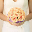 This arrangement has the calm, lyrical quality of a bridal daydream: a symmetrical cluster of apricot roses at the centre, each petal curling outward in soft spirals that glow from within, like warmed porcelain. Encircling those roses is a ring of purple-tinted lisianthus-white at the throat with violet edges-that provides an elegant cool counterpoint to the peach warmth, reminiscent of evening light over Tufnell Park Playing Fields. Scattered sparingly through the composition, fine sprays of white baby's breath create a subtle lattice, lending weightless texture and the sense that the bouquet might float on a summer breeze. The palette reads as creamy, powdery, and refined; under diffused studio or morning light the petals show delicate translucence and gentle shadowing that emphasizes the careful placement of every bloom. I craft bouquets like this for couples who walk from nearby Junction Road or who book intimate ceremonies in Dartmouth Park's green corners, imagining the flowers held against lace or a simple silk gown. Scent is understated-fresh rose with green, dewy notes-and the feel is plush yet light in the hand, balanced for comfort during vows and photographs. Flowers Tufnell Park prepares designs like this with attention to bloom condition and proportion, and we ensure they travel to a venue with stems secure, often available for same-day delivery across Tufnell Park and neighbouring Kentish Town when needed.