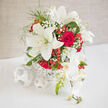 An elegant wedding arrangement glows against a pale, uncluttered backdrop, the flowers gathered with the kind of care you might expect from a florist who knows every corner of Tufnell Park. Dominating the composition are full, creamy white lilies, their star-shaped blooms opening wide and dramatic, each petal slightly curved and luminous, as if brushed by the soft light that filters down nearby streets like Tufnell Park Road and Brecknock Road. Nestled intimately between the lilies, classic red roses sit in layered spirals, their velvety petals offering depth, warmth, and a hint of old-fashioned romance, the sort of feeling you associate with a timeless ceremony in a local church or a civil service in Islington. Drape-like orchid blooms in a pale, almost translucent white trail gently over one side of the bouquet, creating a graceful cascade that catches tiny reflections of light, adding a luxurious, flowing movement. Fine flecks of gypsophila weave through the structure, creating a soft, cloudlike veil that bridges the strong dialogue between the crimson roses and pure lilies. Bright clusters of red hypericum berries punctuate the design, their glossy, rounded forms suggesting festive glasses raised in celebration after the ceremony in a nearby Tufnell Park venue. As a whole, the palette is crisp and refined-ivory, scarlet, and scattered hints of coral-yet the textures remain touchable and layered, from satiny rose petals to the delicate frill of baby's breath. This is a bouquet that balances tradition with modern styling, ideal as a centerpiece for a wedding reception in a north London townhouse or as a dramatic bridal display, ready for careful delivery to homes and venues across Tufnell Park and the surrounding N19 area.