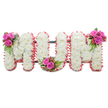 A carefully composed standing tribute that spells out MUM in three large, connected capital letters, photographed against a clean white backdrop so every detail reads clearly. Each letter is formed from a dense carpet of small, snow-white chrysanthemums whose tightly packed heads create a soft, cushiony surface and a uniform, serene texture across the whole piece. The outer edges of each letter are gently trimmed with a ruffled, pale pink ribbon or fabric that gives a tender, motherly warmth against the cool white of the blooms. Between the letters a discreet dark green support frame is visible, giving the arrangement its upright, cohesive profile. To punctuate the purity of the chrysanthemums, three vivid accent posies have been artfully placed: a cluster of rich fuchsia-pink roses, glossy fern-like greenery and tiny reddish-orange hypericum berries nestles on the upper left shoulder of the first M; a matching posy sits in the curved base of the U; and a final coordinated cluster adorns the upper right of the second M. The combination of feathery white mums, velvety pink roses, and bright berries produces a calming visual rhythm, with subtle differences in bloom stage and texture that catch soft light and offer gentle shadowing. As a florist who arranges sympathy flowers for funerals and memorials in and around Tufnell Park and nearby Dartmouth Park, I see this as a graceful, traditional expression of love and remembrance-quietly scented, dignified in scale, and designed to offer comfort and a beautiful focal point at a service, wake, or graveside farewell.