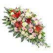 A dignified, double-ended funeral spray stretches across a white background, its long, tapered shape designed to lie gracefully along the top of a coffin. The arrangement is luxuriously full, with flowers placed so close together that the foliage forms a soft, supportive cradle beneath them. At the heart of the design, rich red Oriental lilies open wide, their star-shaped blooms and prominent stamens creating striking focal points that symbolise strength and devotion. Around these, a generous selection of roses in cream, ivory, and the palest pink form gentle clusters, some still in bud, others fully open, their layered petals suggesting tenderness and enduring affection. Pale pink spray carnations ripple through the piece, their frilly edges adding softness and volume. Among the pastel hues, small white chrysanthemum and daisy-like flowers glimmer like scattered stars, bringing brightness and a sense of quiet hope. Cool-toned accents of blue-purple thistles and tiny lavender filler flowers add texture and contrast, giving subtle depth and movement to the overall composition. The whole spray rests on a base of dark, glossy leaves and lighter, feathered greenery that stretches outward at both ends, creating an elegant silhouette that narrows gently towards the tips. The mood is one of calm respect and heartfelt sympathy, the kind of arrangement that might be chosen by families from around Tufnell Park, Dartmouth Park, or nearby Kentish Town for a final farewell. Crafted with the careful eye of a local florist, it feels like a personal tribute, thoughtfully designed to honour a loved one and to offer quiet comfort during a funeral or memorial service.