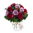 A generously rounded bouquet of freshly cut roses where deep, velvety crimson and burgundy blooms sit cheek-by-jowl with soft lavender and dusty lilac roses, each petal unfurling in layers that catch the light like satin. The flowers are arranged densely, almost mosaic-like, so the two colour families read as a single, harmonious field - the warm, almost ruby reds set against the cool, powdery purples. Interwoven throughout the heads are sprigs of glossy, dark green foliage - the elongated, leathery leaves of ruscus or salal - that give the composition depth and a green framework for the blooms to breathe. Scattered playfully among the roses are small, bright red-orange rose hips that add a rustic, tactile contrast: firm, shiny berries that break the velvet with a spark of autumnal colour. The bouquet sits in a rounded, bulbous mercury-glass vase whose antique silvered and mottled surface shimmers as it catches soft studio light; the vase narrows slightly at the neck and is finished with a simple band of natural raffia tied into a modest knot. From that tie hangs a small rectangular white gift tag with a hand-drawn floral motif and room for a handwritten message, left intentionally blank in the photo. Set against a brilliant white backdrop, the arrangement's colours and reflective textures read with exceptional clarity and freshness. This is a bouquet that reads as romantic and considered - perfect for anniversaries, quiet apologies, or as a luxurious, thoughtful gift to brighten a north London flat near Tufnell Park tube or a cosy maisonette on Fortess Road.