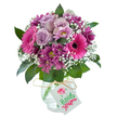 A captivating floral bouquet, overflowing with lush tones of soft lavender, vibrant fuchsia pink, and rich plum, stands proudly against a crisp white background-evoking the charm of Tufnell Park's neighbourhood celebrations. At the heart, tender pale purple roses bloom elegantly, surrounded by striking gerbera daisies in shades of hot pink, each with a dramatic dark centre, symbolising joyful moments shared along Fortess Road. Smaller, velvety magenta chrysanthemum blossoms nestle between the stars of the arrangement, their yellow-green eyes adding depth and intrigue. Wisps of delicate white baby's breath scatter throughout, lending lightness and a feathery, cloud-like texture, reminiscent of the peaceful morning air along the leafy paths of Tufnell Park. Lush dark green foliage supports the blooms, offering a fresh, vibrant contrast. The bouquet is presented in a rounded, clear glass vase whose surface gleams with a subtle crackled finish, the whole tied simply with natural raffia. A small, white gift tag is thoughtfully attached, inviting a message of celebration or affection-whether for a birthday, anniversary, or just to let someone know they are appreciated. Radiating with colour, scent, and warmth, this bouquet encapsulates the heartfelt artistry of Tufnell Park's florists, a gift equally suited to brightening a home or marking life's special milestones.