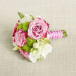 On a neutral, light beige fabric that looks like gently rumpled linen, a small, meticulously crafted bouquet lies as if just set down between photos at a Tufnell Park wedding. The cloth's woven texture forms a calm, natural backdrop, allowing the flowers' colours to glow. Two fully opened roses take pride of place, their petals spiralling outwards with a soft, velvety sheen. At their centres, the pink is delicate and powdery, gradually intensifying to rich fuchsia and magenta along the outer edges, giving each bloom a painterly depth. Around them, clusters of lime-green button chrysanthemums - those compact, spherical blooms with tightly layered petals - provide a lively contrast, adding brightness and a slightly playful texture that feels contemporary yet timeless. Interspersed white flowers, some open and star-like with slender petals and pale yellow-green hearts, others still enclosed as creamy buds, lend an air of purity and gentle movement, reminiscent of lisianthus or freesia often used for bridal work along Campdale Road and Fortess Road. Slim green stems and the occasional leaf peek through, suggesting careful yet relaxed arranging. The stems are cut short and banded into a neat, easy-to-hold handle. This handle is wrapped in a smooth, fuchsia-pink satin ribbon, its sheen catching the light, then finished with a winding strand of tiny white pearls that loop elegantly along the length, like a delicate bracelet. The result is a mini-bouquet that feels fresh, romantic, and intimate, perfect as a groom's boutonnière, a wrist corsage adaptation, or a petite bridesmaid posy for celebrations across Tufnell Park and the surrounding streets.