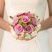 The essence of bridal romance shines in this carefully styled bouquet, photographed against the intricate ivory lacework of a Tufnell Park bride's gown. At the bouquet's center, luxurious mauve roses bloom in full, their ruffled petals deepening to a radiant fuchsia at the edges, each one exuding the tenderness of a new love in spring. Tucked among these velvety blooms are chartreuse-green chrysanthemums-button-like and fresh-hinting at the verdant street gardens and parks that colour the fabric of Tufnell Park. Flowing outward from the heart of the arrangement, a soft crown of petite white flowers-scented freesia or dainty spray roses-lends an ethereal, almost frosted finish, accented with specks of fresh green buds. The bride's hands, nails painted blush and graced with a subtle glimmer on one finger, clasp the stems gently, encapsulating the fragility and promise of the occasion. The gentle, diffuse lighting gives the scene a sense of calm anticipation, highlighting every detail and texture-the filigreed lace, verdant greens, and rosy hues. It's a bouquet that evokes the unique blend of elegance, community, and artistry found in weddings across Tufnell Park, inviting dreams of celebration and enduring love.