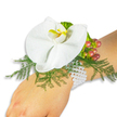 A delicate white Phalaenopsis orchid sits at the centre of a wrist corsage, resting on the light-skinned wrist of the wearer against a clean white backdrop. The orchid's broad, satiny petals fan open like a quiet, luminous moth; its labellum offers a small, vivid wash of yellow graduating into a hint of orange that catches the light and draws the eye. Beneath and around the bloom a fluff of feathery asparagus-fern creates soft, airy texture in bright green tones, the fine fronds lifting and almost floating above the skin. To the upper right, a tight cluster of glossy Hypericum berries reads like a little story of colour-pale green at the stem, blushing through rose to a deep cranberry-while a ruffled, lime-green accent leaf slips in beside them to add a fresh zing of contrast. The arrangement is secured to the wrist with a multi-strand bracelet of small white pearls whose cool, lustrous surfaces nestle against the skin and give the piece a timeless, heirloom feel. The overall composition is quiet and romantic, a study in contrasts: smooth and satiny orchid petals against lacy greenery and rounded, glossy berries. In softer daylight the mix of textures suggests a whisper of perfume and the gentle rustle of fern fronds. As a local florist would explain, this corsage reads as classic and understated-ideal for a wedding, prom, or any event where a single refined accent is desired. It evokes walks from Tufnell Park station toward Dartmouth Park, where fresh seasonal stems are gathered, and it reflects careful hand-assembly and floral restraint familiar to the neighbourhood's tastes.